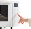 A hand is pressing a button on the control panel of a white microwave. Produktbild-Vorschau