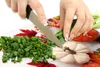 A person is chopping green onions on a cutting board with a knife. There are decorative pumpkins and autumn leaves on the cutting board. Náhled obrázku produktu