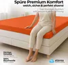 A woman sitting on an orange fitted sheet on a bed. Produktbild-Vorschau