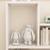 Two Baymax figures are displayed on a white shelf, with books and a small radio on adjacent shelves. Náhľad obrázku produktu