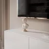 A white bust sculpture sits on top of a white cabinet, with a television screen in the background displaying text. Voir les images du produit