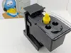 A close-up of a printer maintenance tool, likely for cleaning print heads, with a cartoon image in the background. Produktbild-Vorschau
