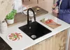 A modern kitchen scene with a black granite sink, a person preparing food, and another person holding a cup of coffee. Produktbild-Vorschau