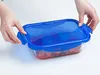 Hands are shown closing the lid on a transparent glass food storage container with a blue lid. Anteprima dell’immagine prodotto