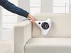 A hand is using a white handheld vacuum cleaner to clean a light-colored sofa. Produktbild-Vorschau