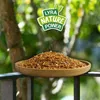 A wooden bowl filled with dried shrimp sits on a railing, with a blurred green background of trees and foliage. A logo with text is visible at the top. Produktbild-Vorschau