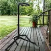 A black guitar stand is placed on a wooden deck outdoors, with a grassy lawn and trees in the background. Náhľad obrázku produktu