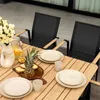 A table setting with plates, cutlery, and food on a wooden table, with chairs in the background. Produktbild-Vorschau
