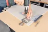A person is using a power drill and a jig to drill holes in a cabinet door for a hinge. Voir les images du produit