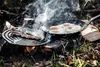 Cooking eggs and bacon over a campfire using a cast iron pan and grill. Produktbild-Vorschau