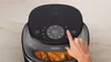 A close-up shot of an air fryer with a hand pressing a button on the control panel. There is food inside the air fryer. Produktbild-Vorschau