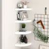 Four white corner shelves are mounted on a light gray wall, decorated with books, a plant, and bottles. Produktbild-Vorschau