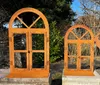 Two decorative metal window frames with an arched top, placed outdoors on stone pedestals, with trees and foliage in the background. Produktbild-Vorschau