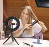 A young woman is straightening her hair in front of a ring light setup, with makeup products on the table. Produktbild-Vorschau