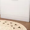 A close-up view of the bottom of a white cabinet and a round, woven rug with a circular pattern on a wooden floor. Podgląd zdjęcia produktu