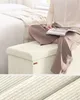 A person sitting on a storage ottoman next to a bed. Náhled obrázku produktu