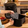 A person is placing a basket into a black air fryer in a kitchen setting. Produktbild-Vorschau