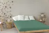 A bedroom scene with a bed, pillows, a side table, and a chair. Produktbild-Vorschau