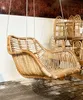 A rattan hanging chair is displayed in a store or showroom, with other rattan furniture in the background. Produktbild-Vorschau