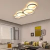A modern living room with a sectional sofa, coffee table, and artwork on the wall, illuminated by a contemporary ceiling light fixture. Produktbild-Vorschau