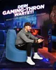 A man is playing a video game while sitting on a large blue beanbag chair in a dimly lit room. Produktbild-Vorschau
