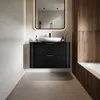 A modern bathroom vanity with a black ribbed cabinet, white sink, and a large illuminated mirror above. The vanity is set against a tiled wall and a wooden accent wall, with a bathtub visible on the right. Anteprima dell’immagine prodotto