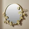A round mirror with a decorative frame of golden ginkgo leaves. Voir les images du produit