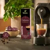 A coffee machine brewing espresso into a glass, with a box of Tchibo Cafissimo Espresso Barista capsules and coffee beans in the foreground. Produktbild-Vorschau