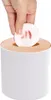 A hand is placing a used cotton pad into a white cosmetic bin with a wooden lid. Náhľad obrázku produktu