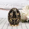 A black and gold decorative egg-shaped toothpick holder sits on a checkered cloth, with white flowers in the background. Náhled obrázku produktu