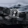 A watch is placed on wet, dark rocks with waves in the background. Voir les images du produit