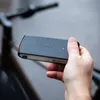 A hand holds a black electronic device in front of a blurred bicycle. Voir les images du produit