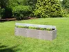 A raised garden bed with plants growing inside, set in a grassy backyard with trees in the background. Voir les images du produit