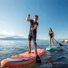 Two people stand-up paddleboarding on a lake with mountains in the background. Produktbild-Vorschau