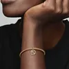 A close-up shot of a person's arm wearing a gold Pandora charm bracelet with a circular zodiac charm. Podgląd zdjęcia produktu