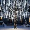 A tree decorated with white meteor shower lights in a snowy yard at night. Produktbild-Vorschau