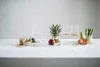 A still life arrangement of glassware and fruits on a white tablecloth, with a white brick wall in the background. Náhled obrázku produktu
