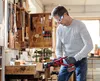 A man in a workshop is using a reciprocating saw to cut a piece of wood. Produktbild-Vorschau