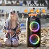 A woman is sitting on a beach holding a smartphone, with a large portable speaker next to her. The speaker has colorful lights. Produktbild-Vorschau