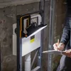 A person is inspecting a wall-mounted toilet cistern with a work light attached. Produktbild-Vorschau