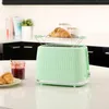 A mint green toaster with a croissant on top, next to a jar of jam and a plate of croissants on a kitchen counter. Podgląd zdjęcia produktu