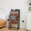 A black metal towel rack with four arms is displayed in a bedroom setting, next to a bed and a white cabinet. Produktbild-Vorschau