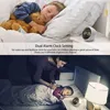 A split image showing a child sleeping with a teddy bear in bed and a mother tucking in another child in a dimly lit room, with digital alarm clocks visible in both scenes. Produktbild-Vorschau