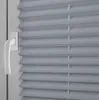 A close-up view of a gray pleated blind with a white handle on a window. Produktbild-Vorschau