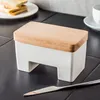 A butter dish with a wooden lid sits on a black tiled surface, with toast and a cup in the background. Podgląd zdjęcia produktu
