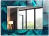 A mirror with a decorative frame of green leaves, reflecting a room with a lamp and a window overlooking trees. Produktbild-Vorschau