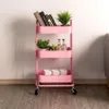 A pink three-tier metal serving cart with wheels, decorated with books, plants, and bottles. Produktbild-Vorschau