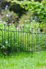 A black metal garden fence borders a lush garden with green grass and blooming flowers in the background. Podgląd zdjęcia produktu