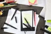 A desk with various stationery items, including pens, notebooks, sticky notes, and papers with diagrams. Produktbild-Vorschau