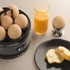 A breakfast scene with an egg cooker, orange juice, an egg in an egg cup, and bread on a plate. Produktbild-Vorschau